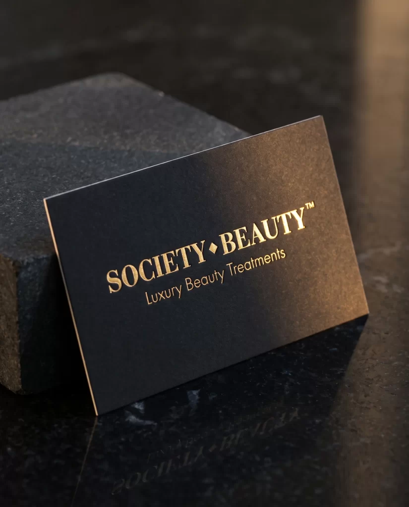 Zwart visitekaartje van Society Beauty met logo in goudfolie op zwart marmer