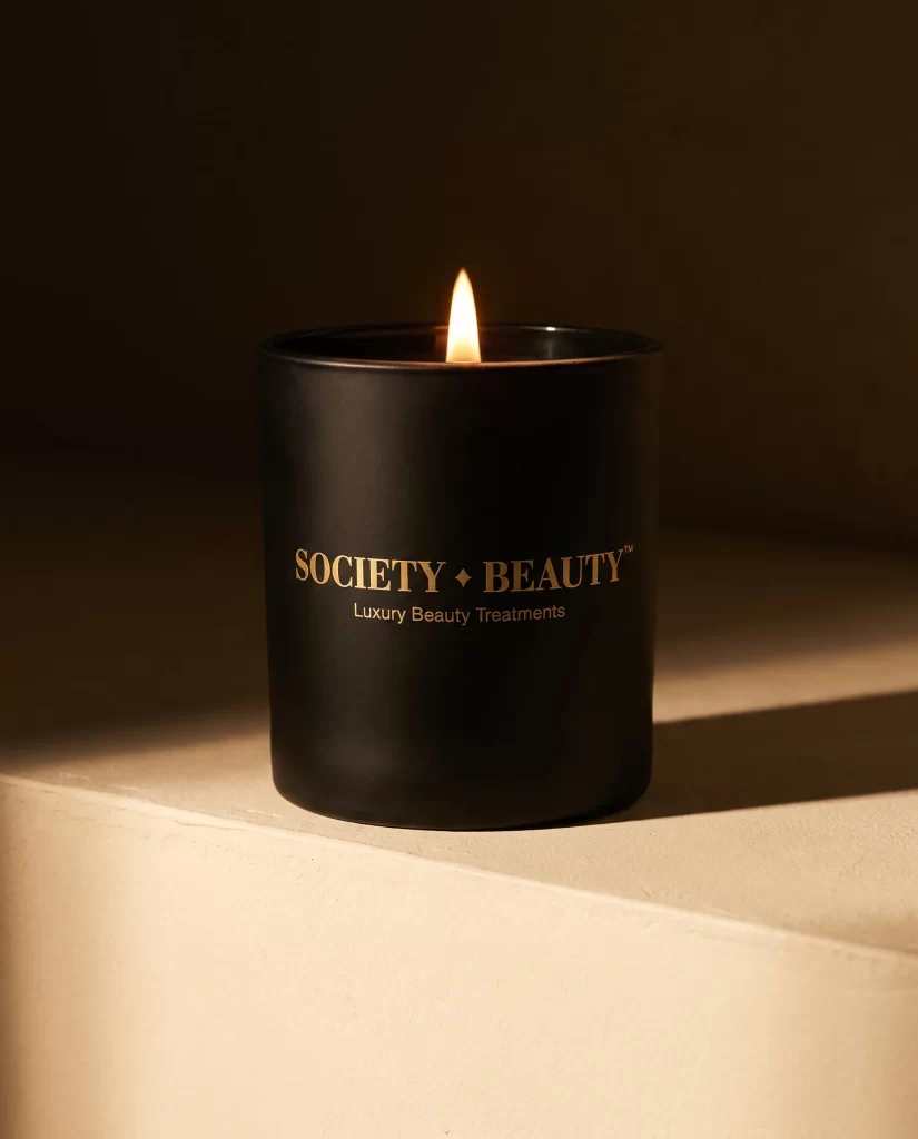 Zwarte kaars met het logo van Society Beauty in goud, in warm zonlicht