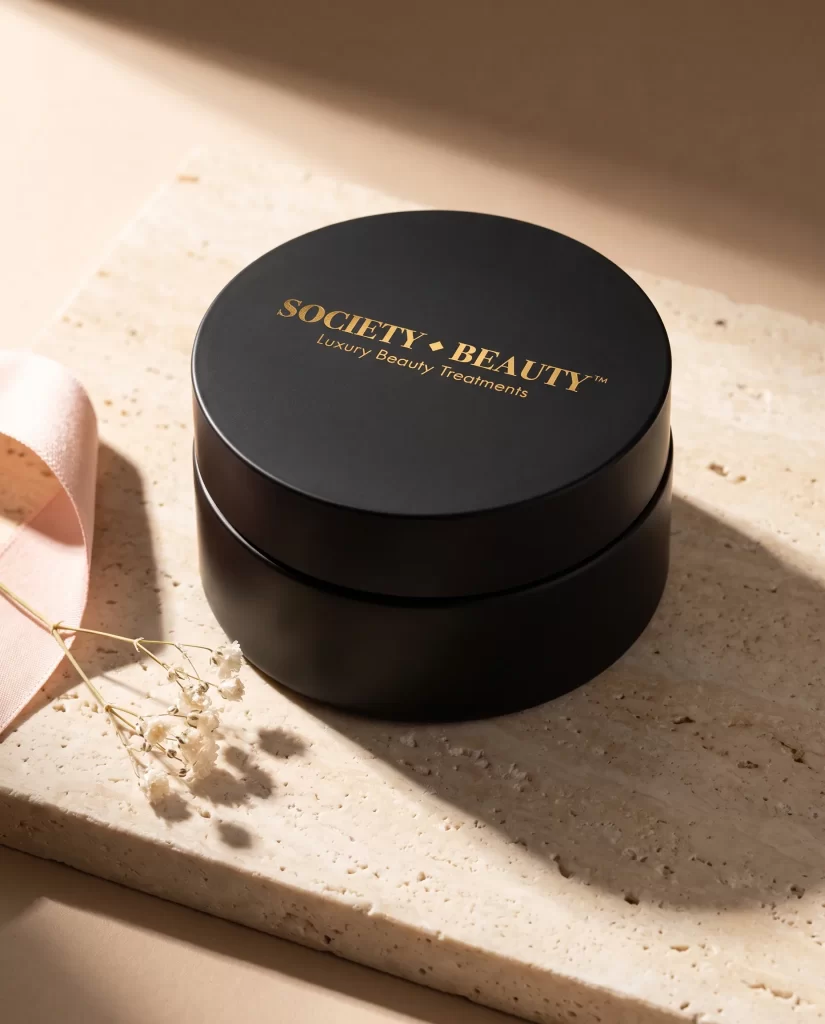 Zwarte crèmepot met het logo van Society Beauty in goudfolie op travertin