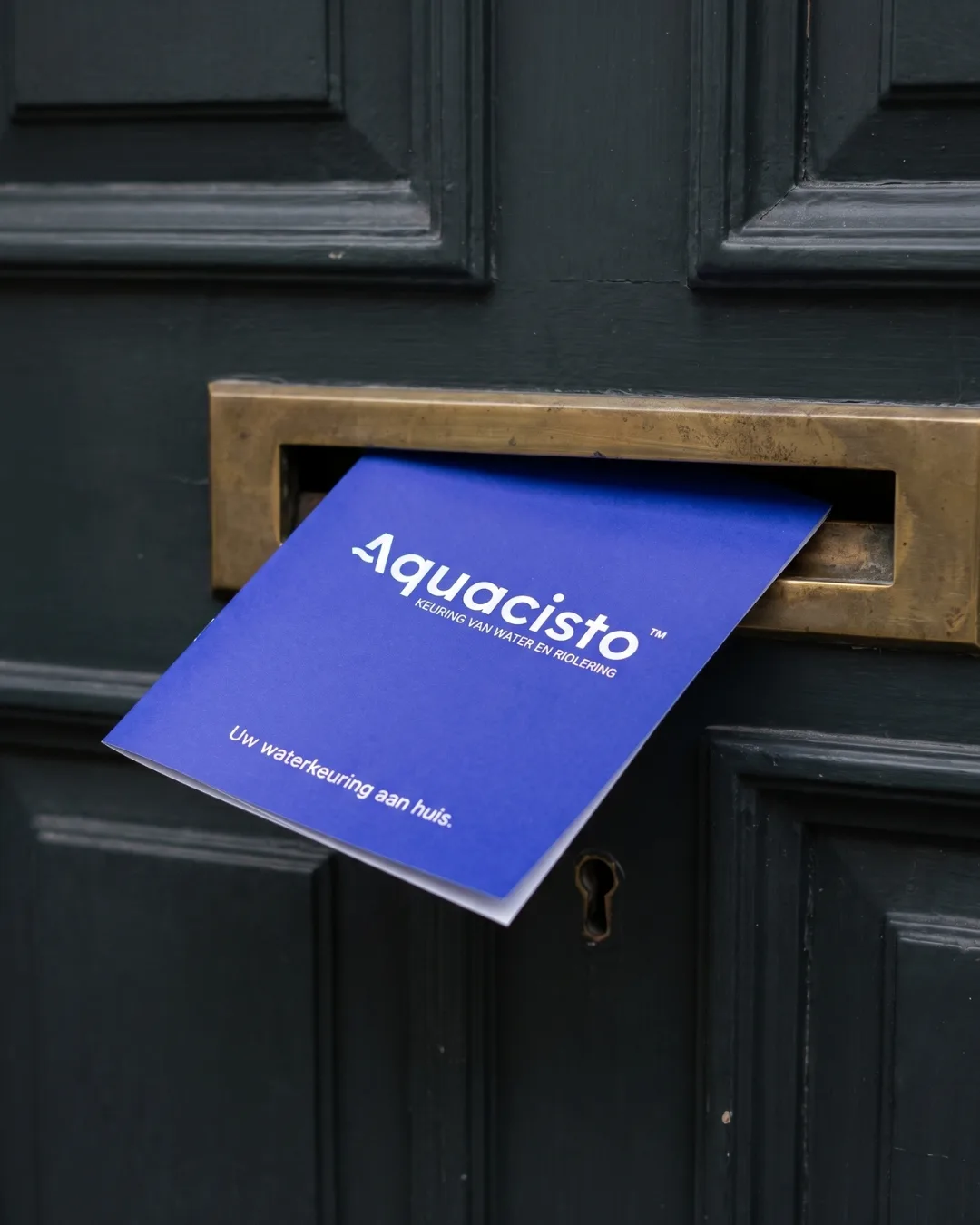 Blauwe folder van Aquacisto met de tekst Uw waterkeuring aan huis in een koperen brievenbus
