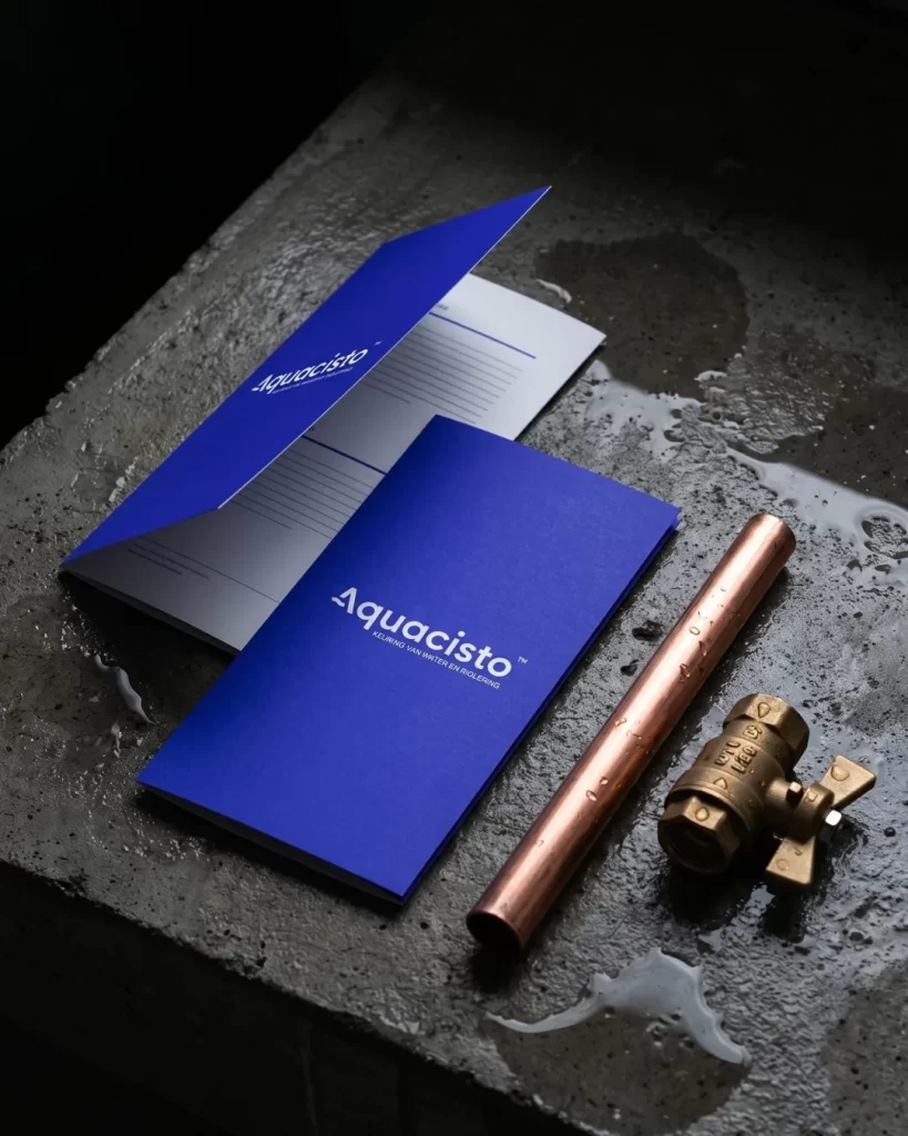 Blauwe brochure en map van Aquacisto naast een koperen leiding en een kraan op natte steen
